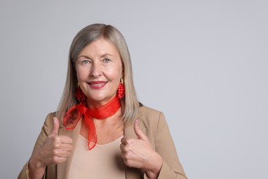 Photo of Senior woman showing thumbs up on light grey background. Space for text