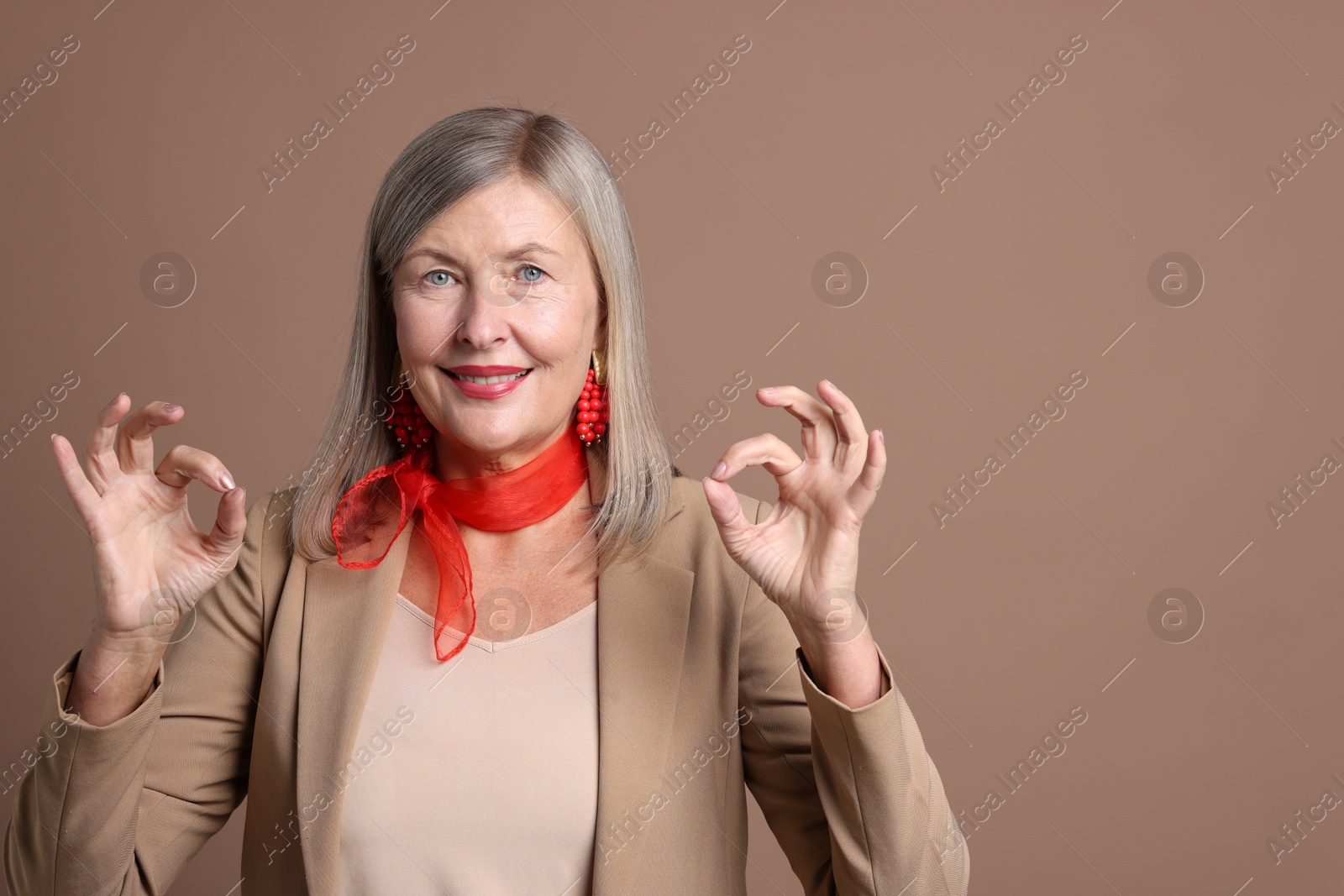 Photo of Senior woman showing okay gesture on brown background. Space for text