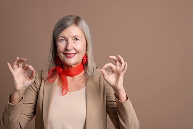 Photo of Senior woman showing okay gesture on brown background. Space for text