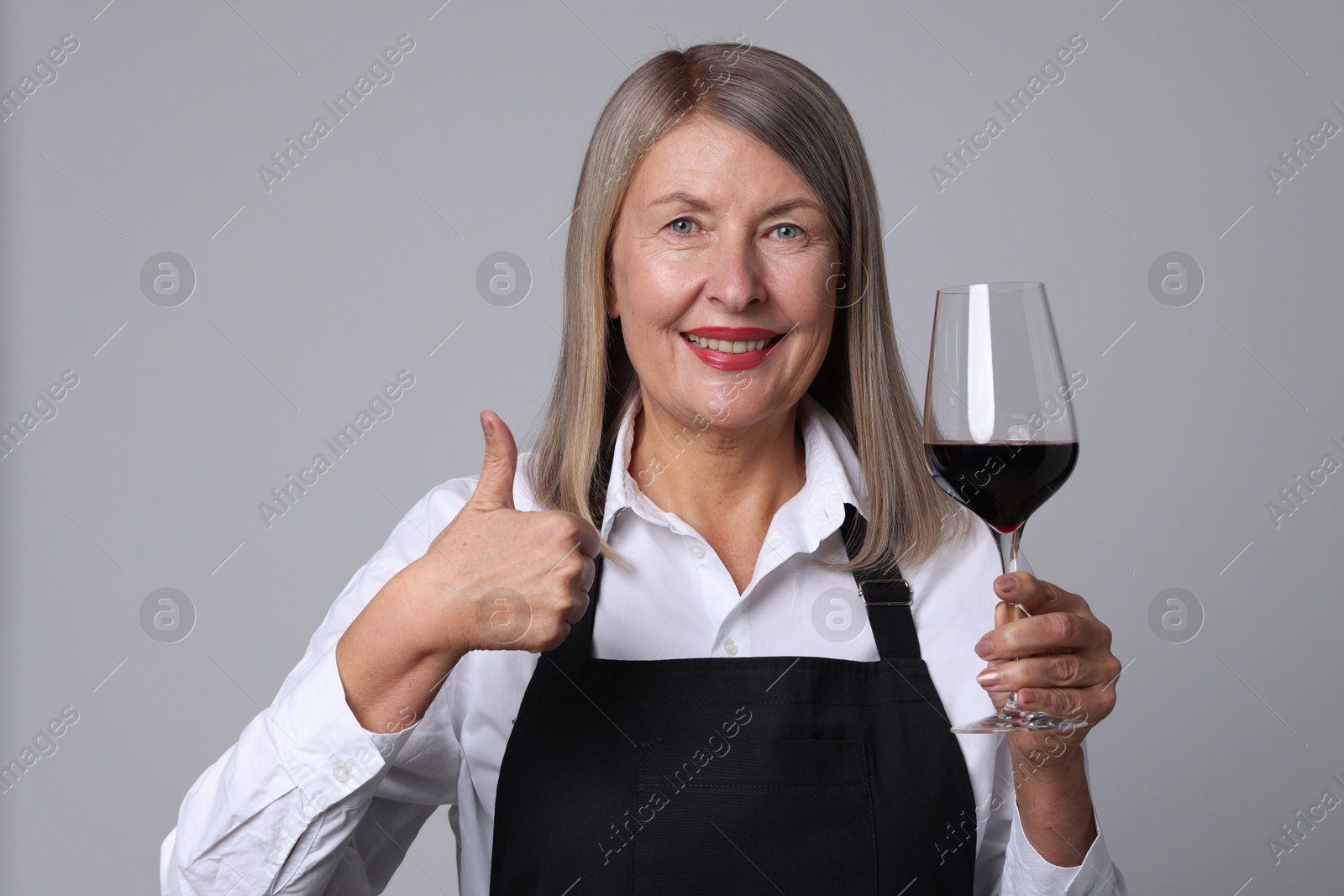 Photo of Senior woman with glass of wine showing thumbs up on grey background