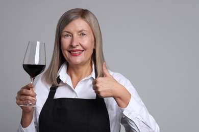 Photo of Senior woman with glass of wine showing thumbs up on grey background