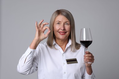 Photo of Senior woman with glass of wine showing okay gesture on grey background