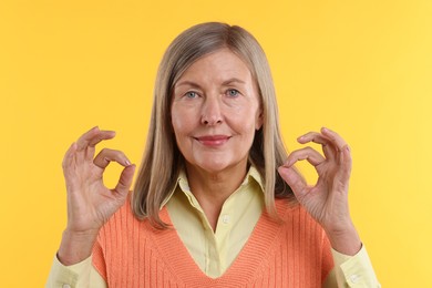 Photo of Senior woman showing okay gesture on yellow background