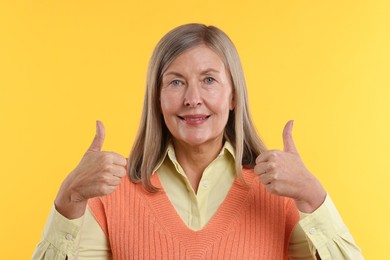 Senior woman showing thumbs up on yellow background