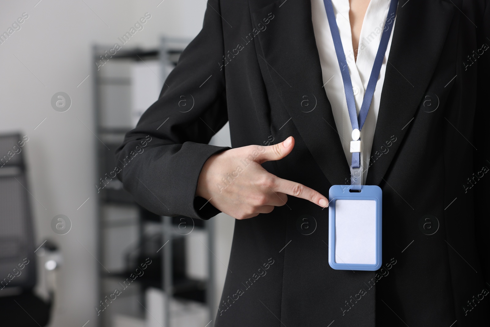 Photo of Woman pointing at her blank badge indoors, closeup