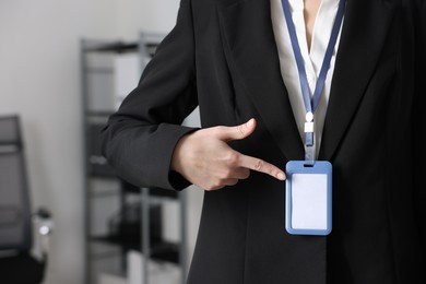 Photo of Woman pointing at her blank badge indoors, closeup