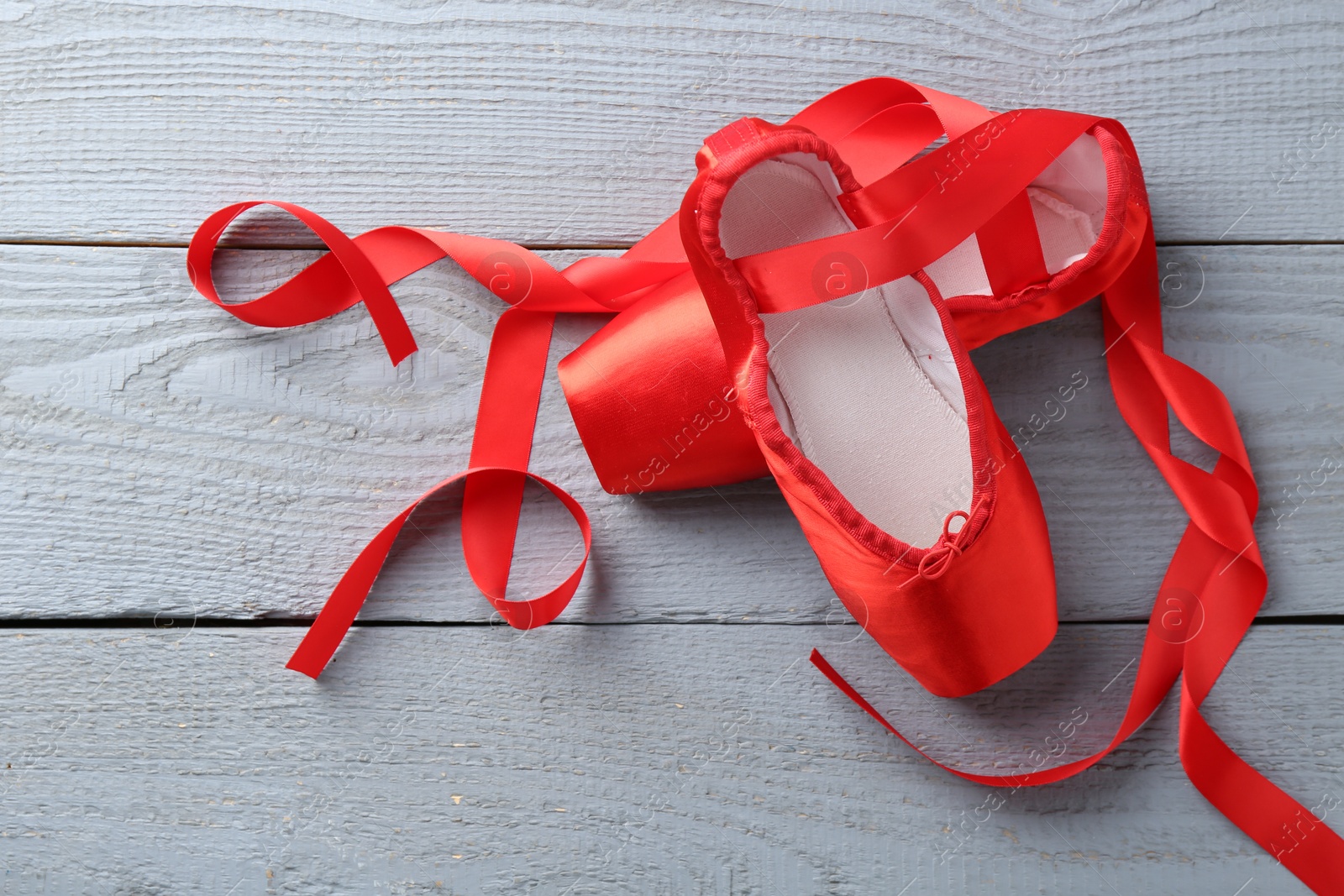 Photo of Pair of red pointe shoes on grey wooden table, top view