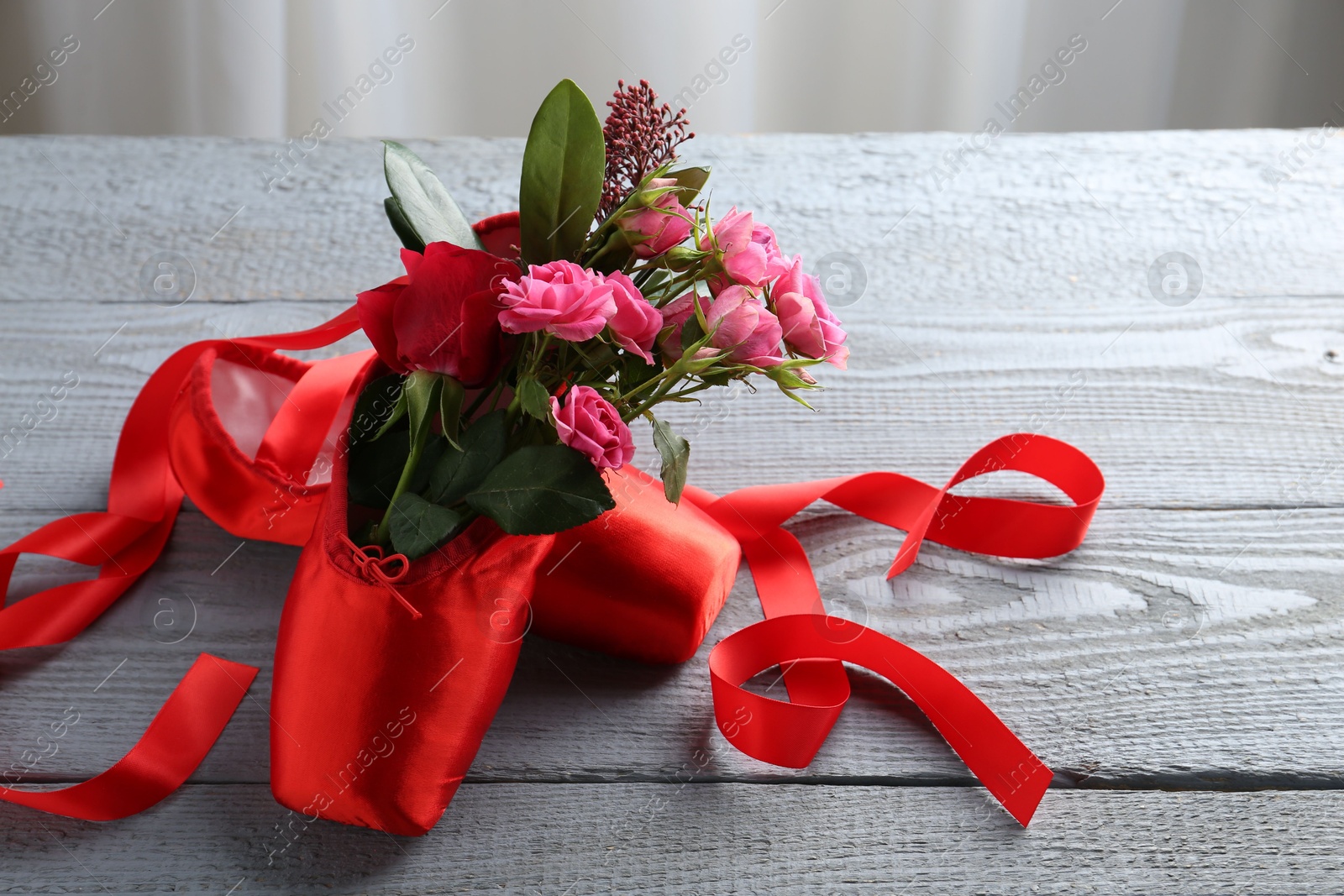 Photo of Pair of red pointe shoes and flowers on grey wooden table, space for text