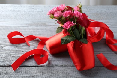 Photo of Pair of red pointe shoes and flowers on grey wooden table