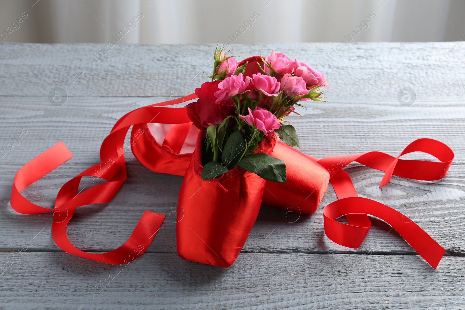 Photo of Pair of red pointe shoes and flowers on grey wooden table