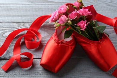 Photo of Pair of red pointe shoes and flowers on grey wooden table, closeup