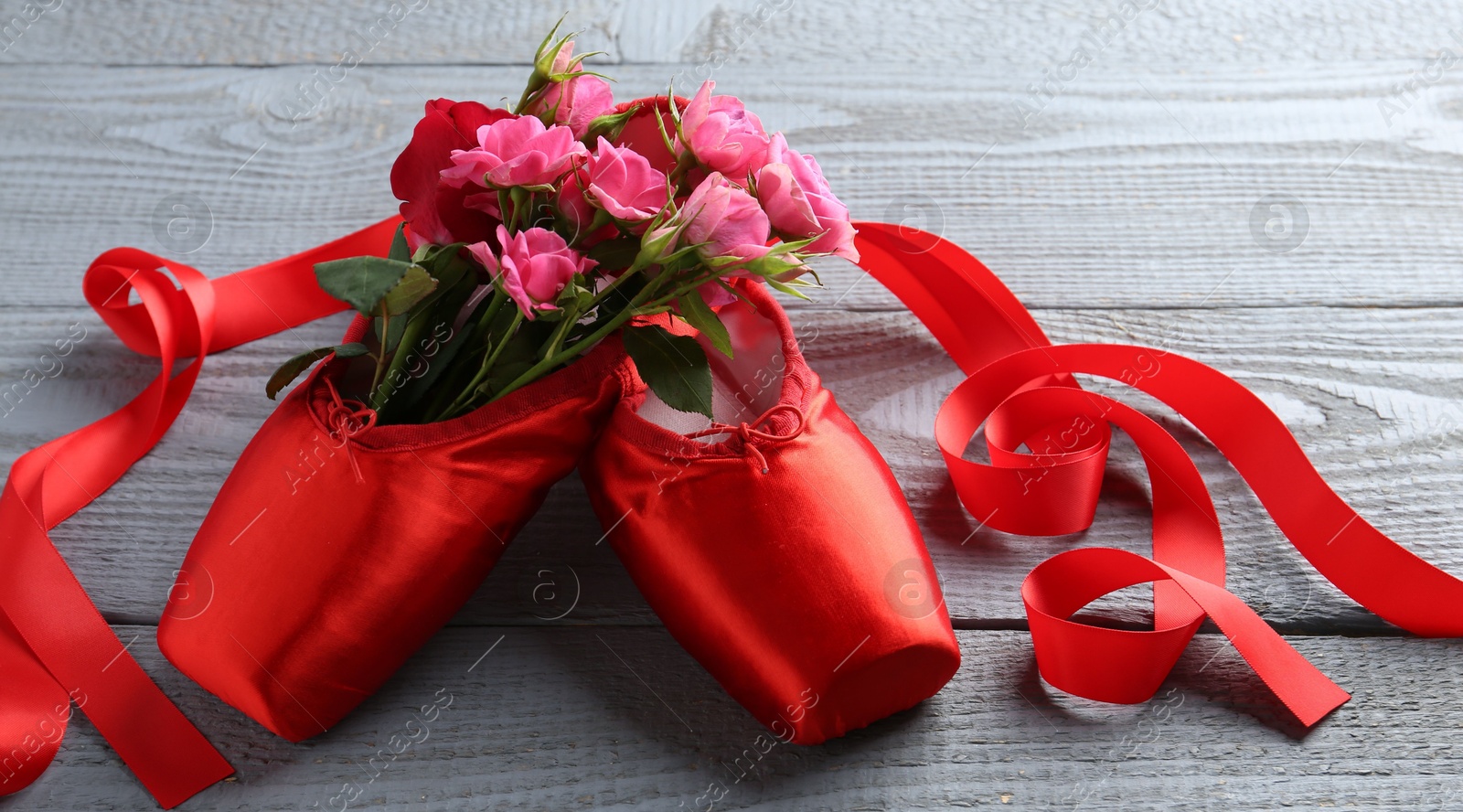 Photo of Pair of red pointe shoes and flowers on grey wooden table, closeup