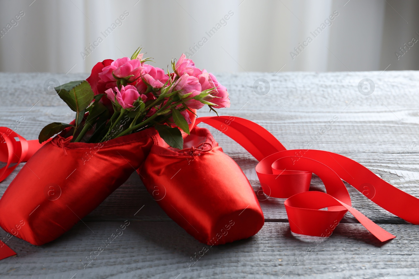 Photo of Pair of red pointe shoes and flowers on grey wooden table