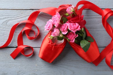 Photo of Pair of red pointe shoes and flowers on grey wooden table, top view