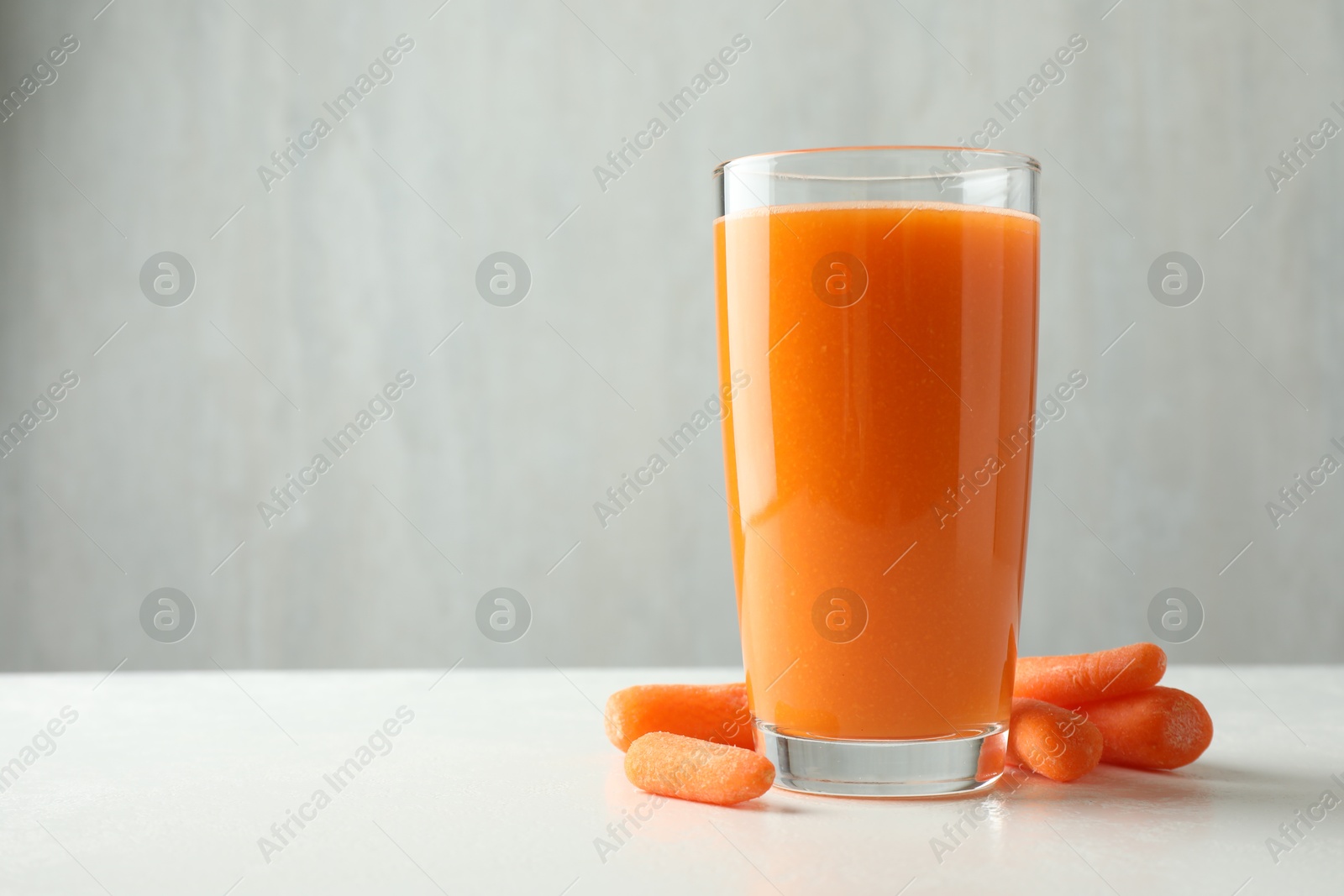 Photo of Fresh carrot juice in glass and vegetables on white table against gray background, space for text