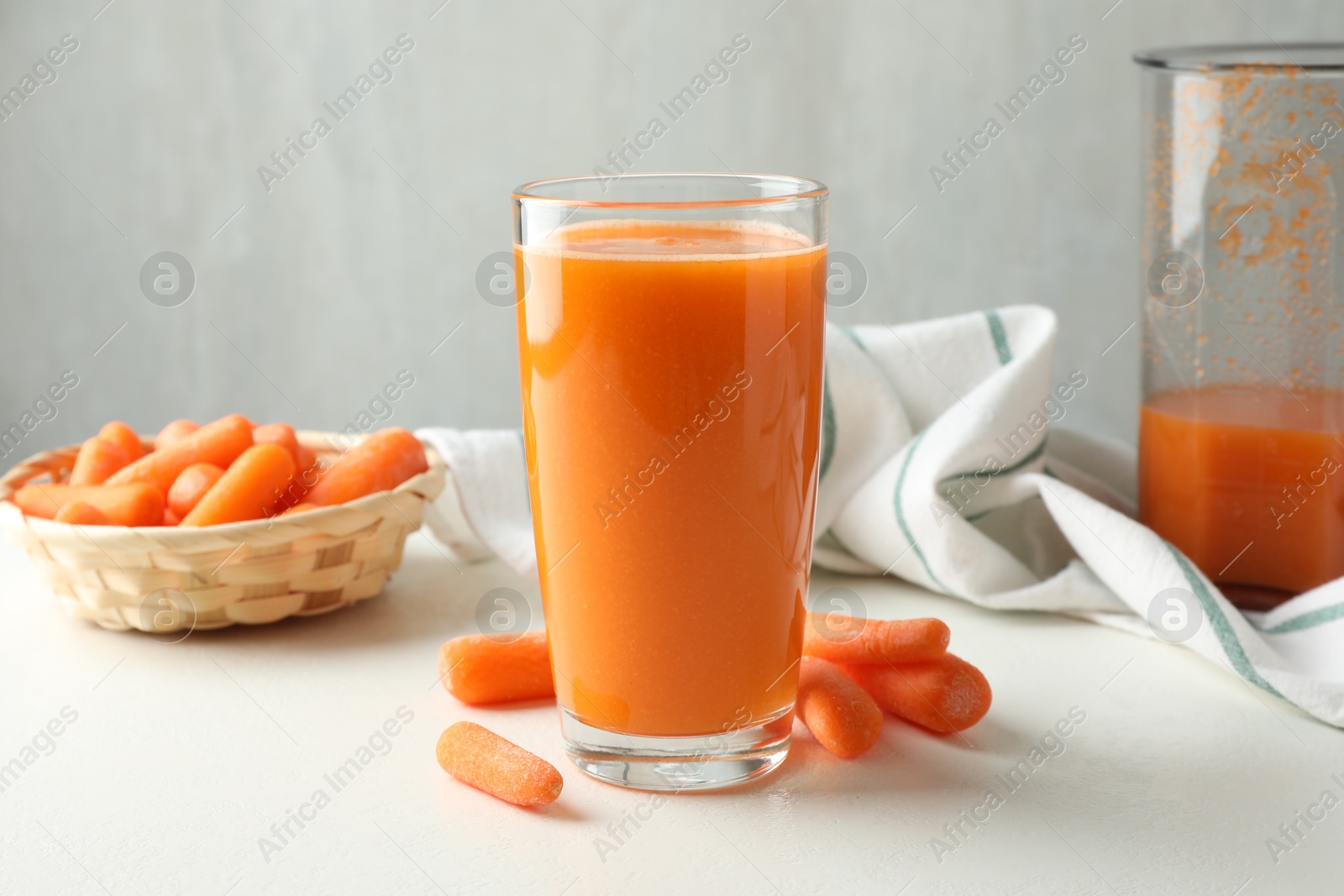 Photo of Fresh carrot juice in glass and vegetables on white table against gray background