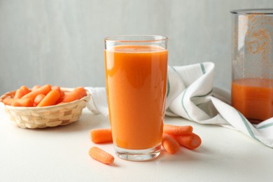 Photo of Fresh carrot juice in glass and vegetables on white table against gray background