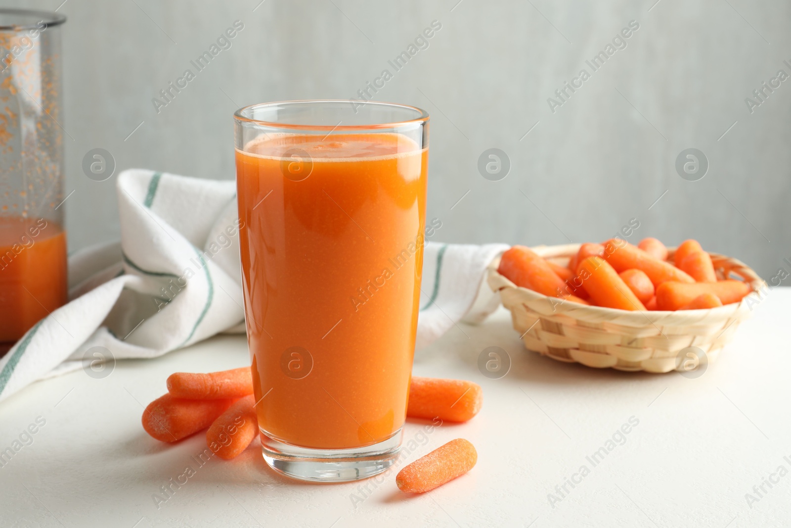 Photo of Fresh carrot juice in glass and vegetables on white table against gray background