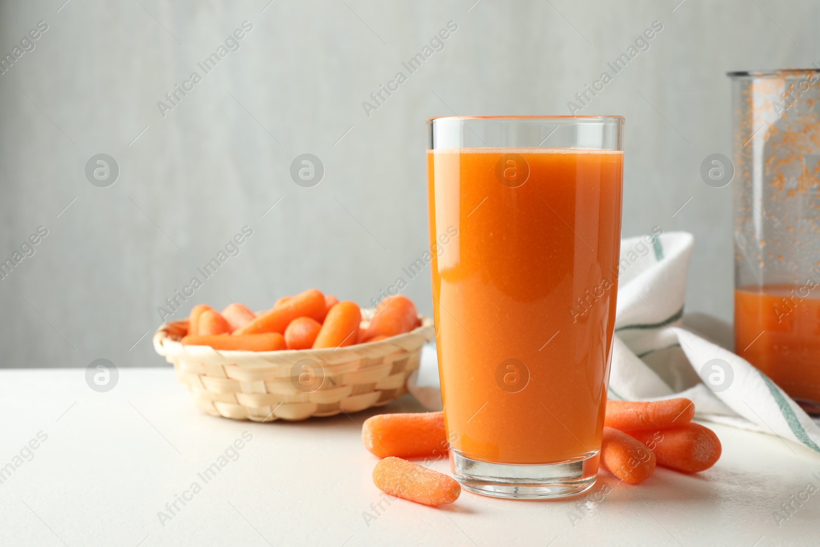 Photo of Fresh carrot juice in glass and vegetables on white table against gray background, space for text