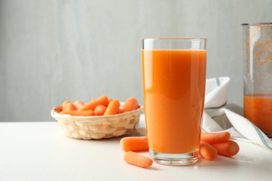 Photo of Fresh carrot juice in glass and vegetables on white table against gray background, space for text