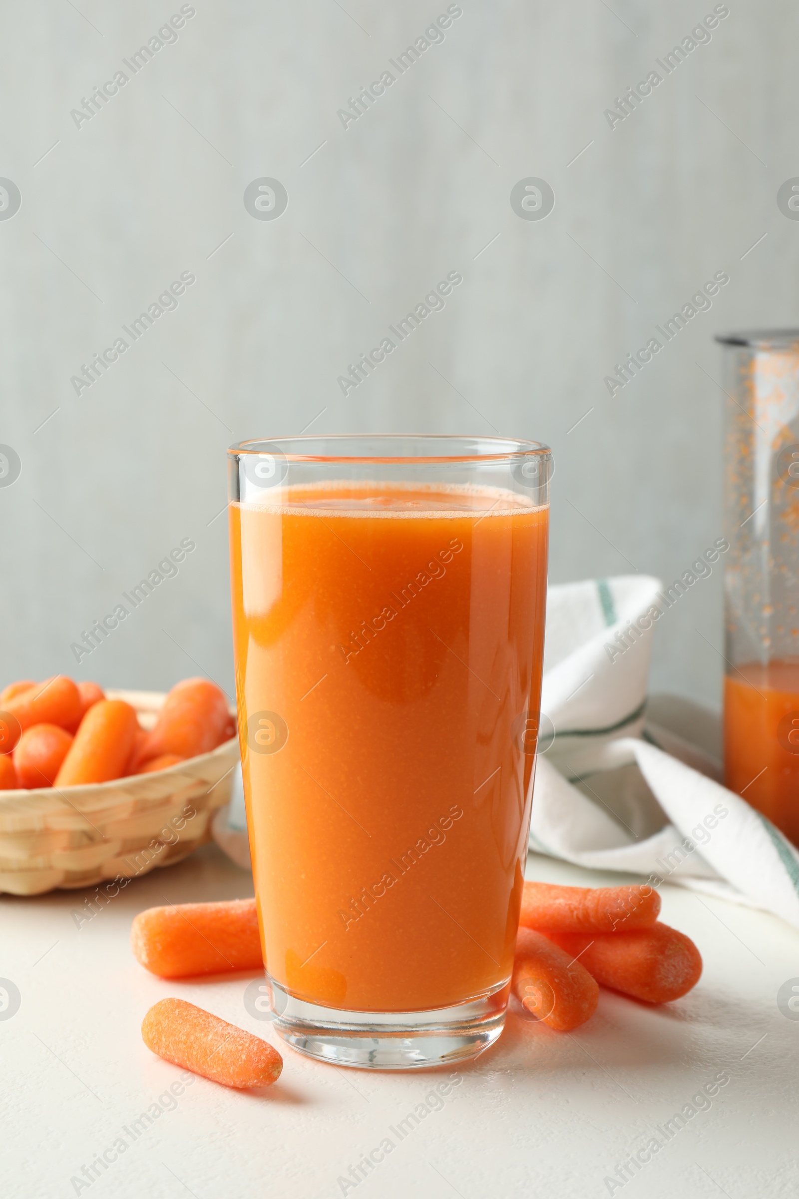 Photo of Fresh carrot juice in glass and vegetables on white table against gray background