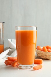 Photo of Fresh carrot juice in glass and vegetables on white table against gray background