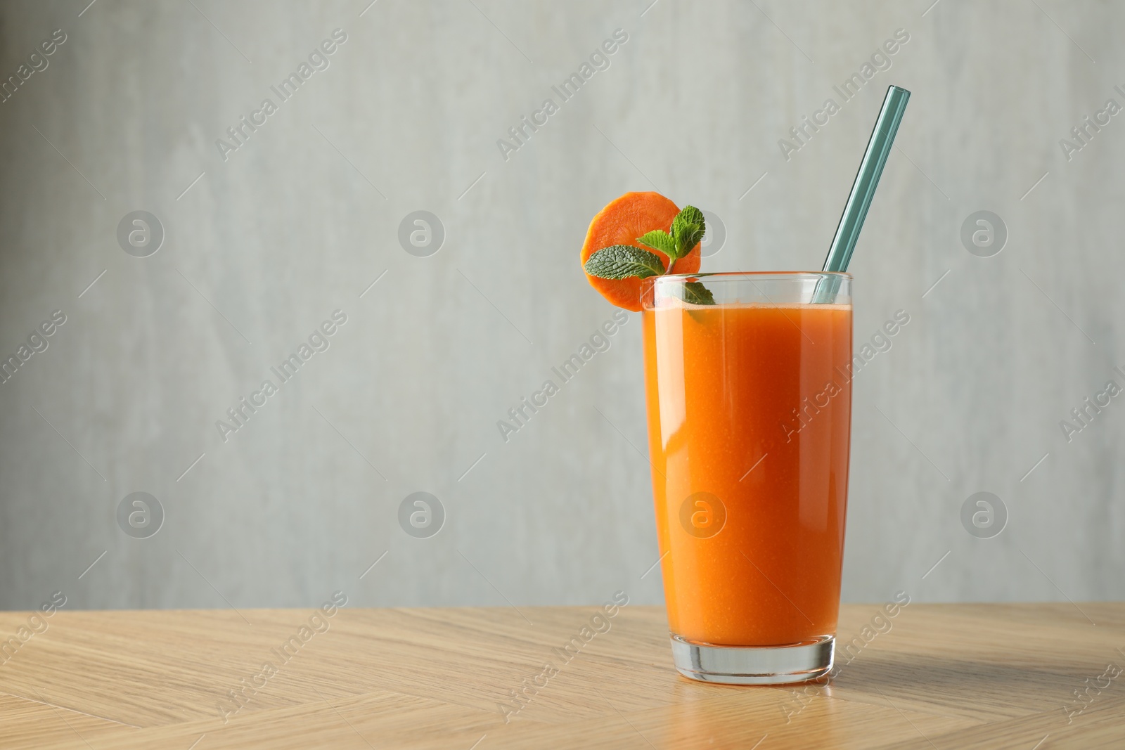 Photo of Fresh carrot juice in glass on wooden table against gray background, space for text