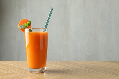 Photo of Fresh carrot juice in glass on wooden table against gray background, space for text