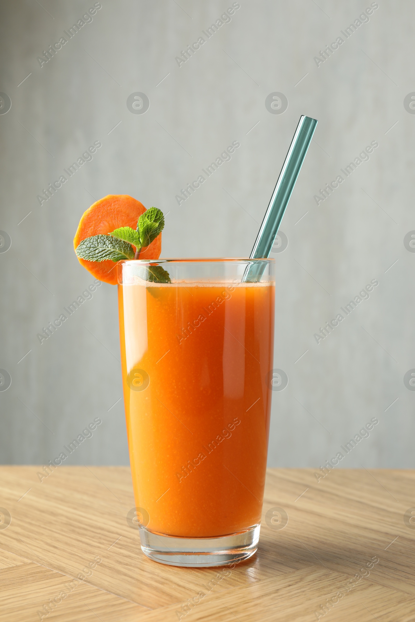 Photo of Fresh carrot juice in glass on wooden table against gray background