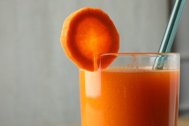 Photo of Fresh carrot juice in glass against gray background, closeup. Space for text