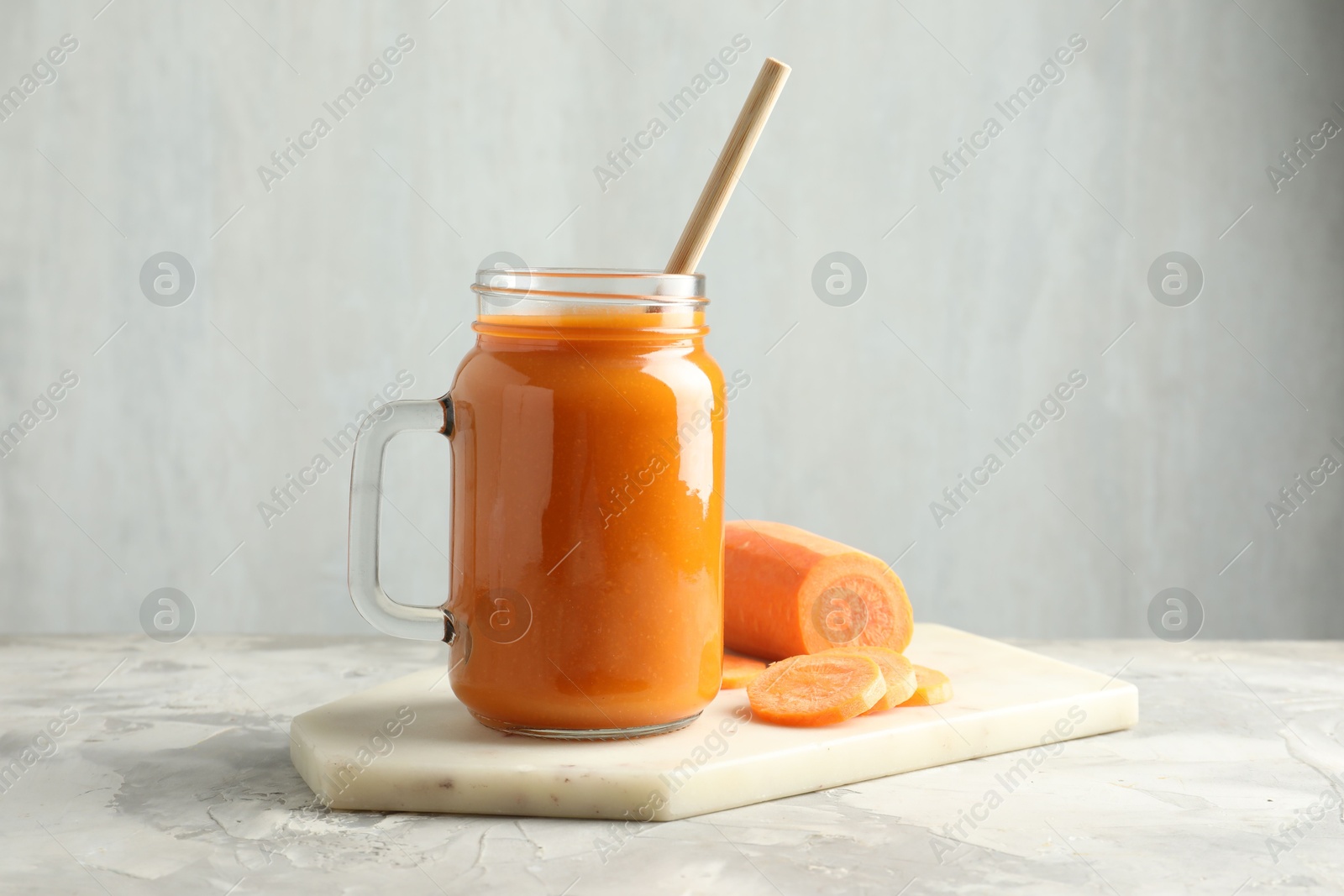 Photo of Fresh carrot juice in mason jar and vegetable on gray textured table