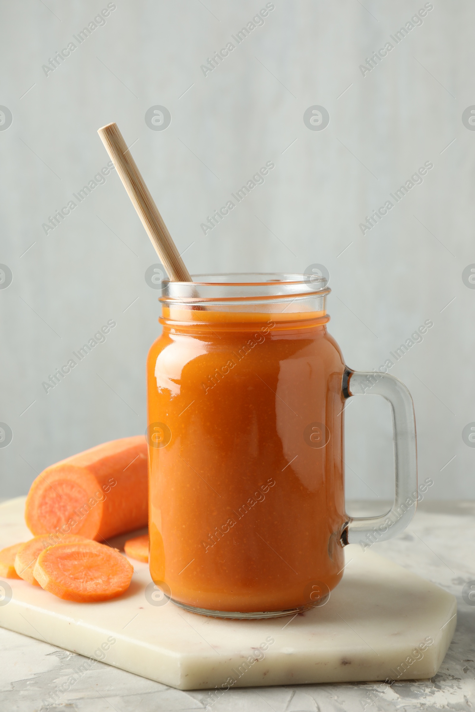 Photo of Fresh carrot juice in mason jar and vegetable on gray textured table