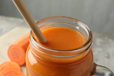 Photo of Fresh carrot juice in mason jar on gray table, closeup