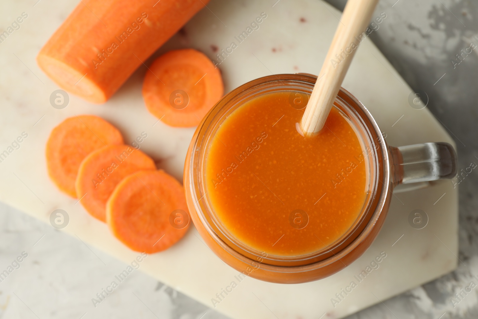 Photo of Fresh carrot juice in mason jar and vegetable on gray table, top view