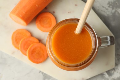 Photo of Fresh carrot juice in mason jar and vegetable on gray table, top view