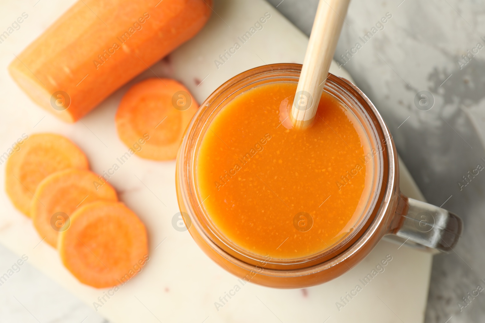 Photo of Fresh carrot juice in mason jar and vegetable on gray table, top view