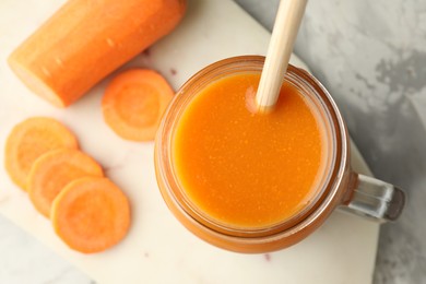 Photo of Fresh carrot juice in mason jar and vegetable on gray table, top view