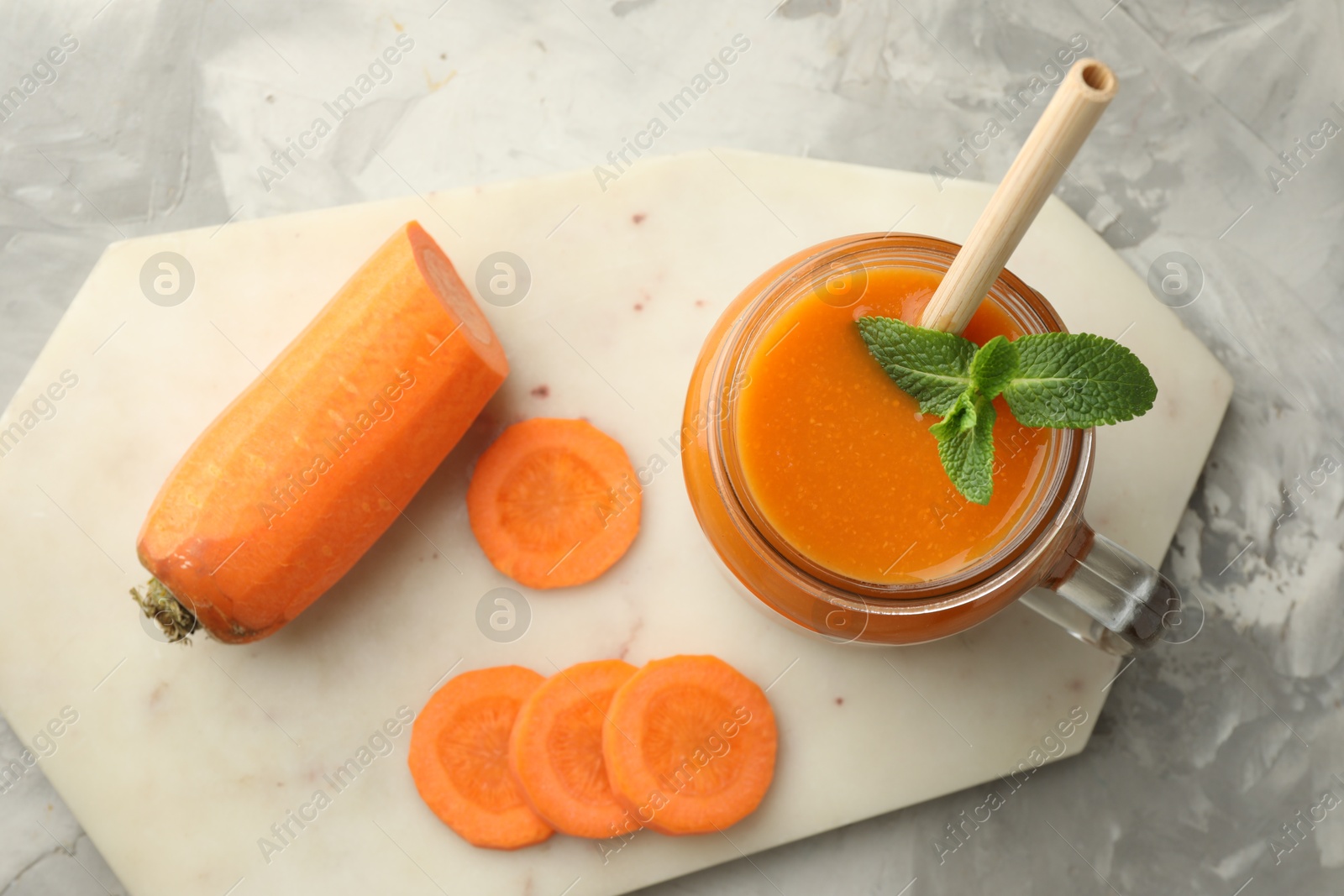 Photo of Fresh carrot juice with mint in mason jar and vegetable on gray textured table, top view