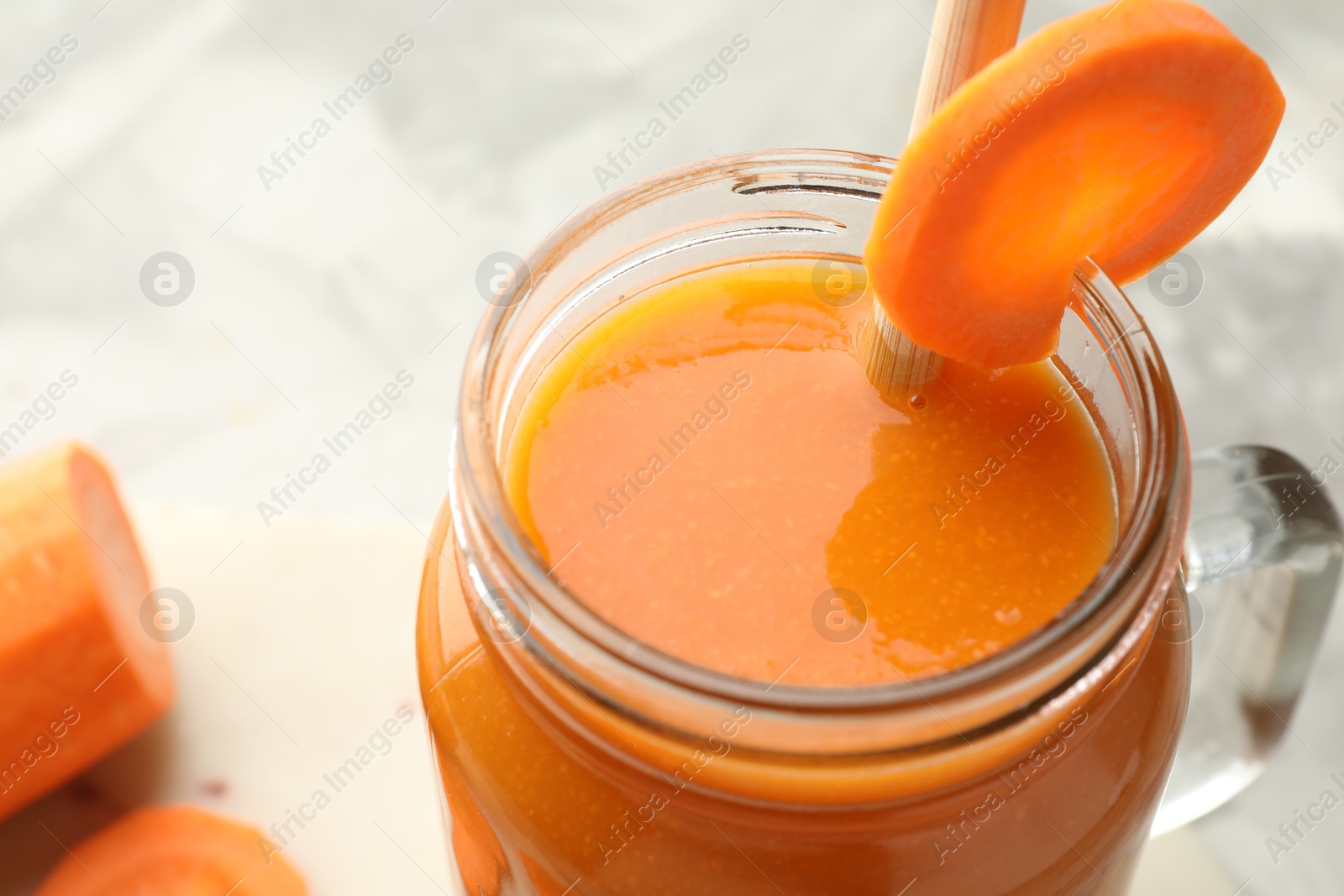 Photo of Fresh carrot juice in mason jar on gray table, closeup