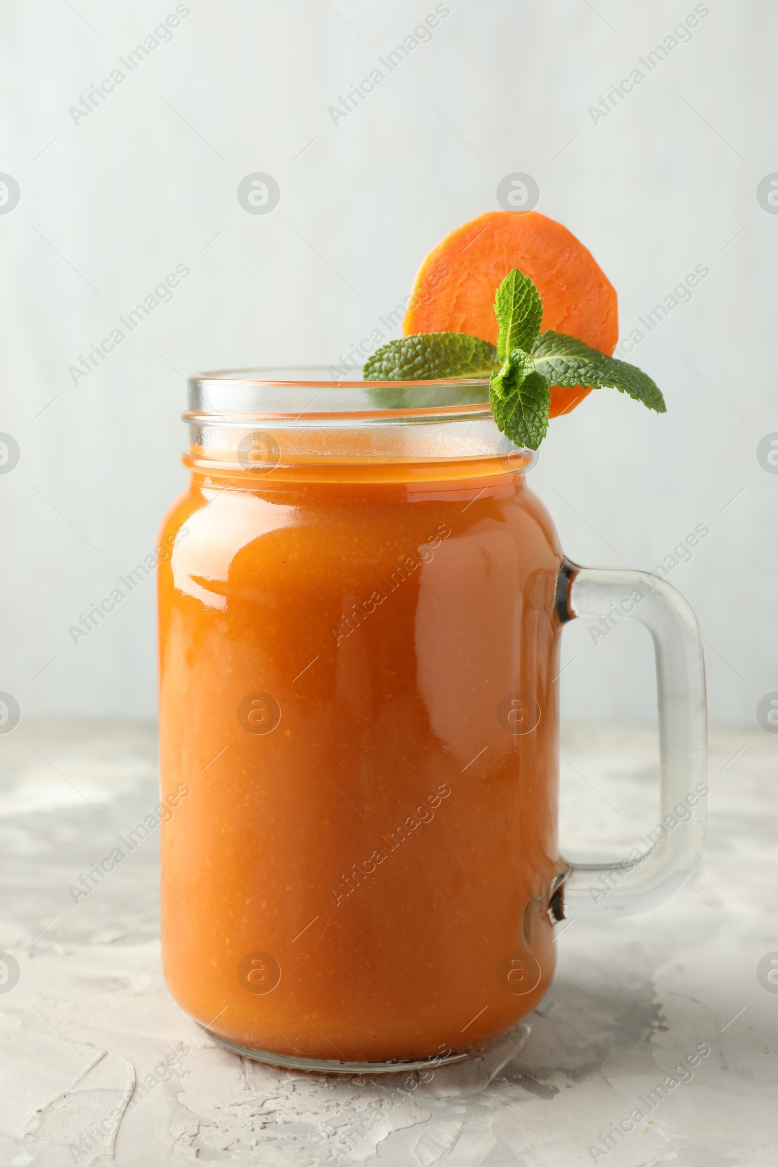 Photo of Fresh carrot juice and mint in mason jar on gray textured table