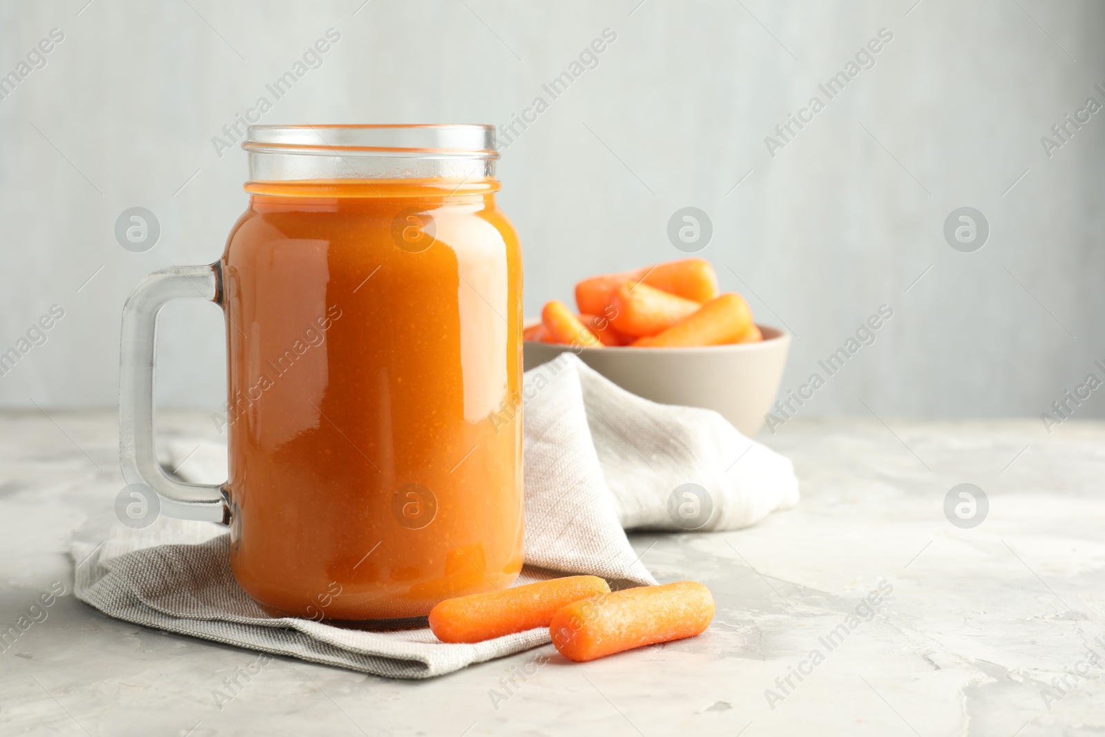 Photo of Fresh carrot juice in mason jar and vegetables on gray textured table