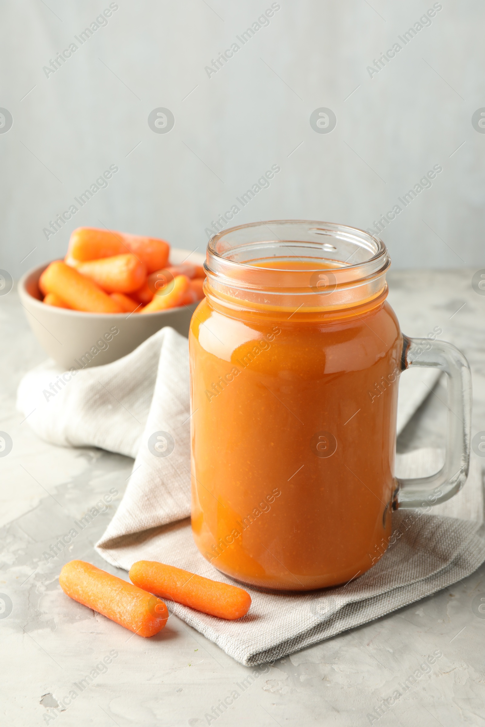 Photo of Fresh carrot juice in mason jar and vegetables on gray textured table