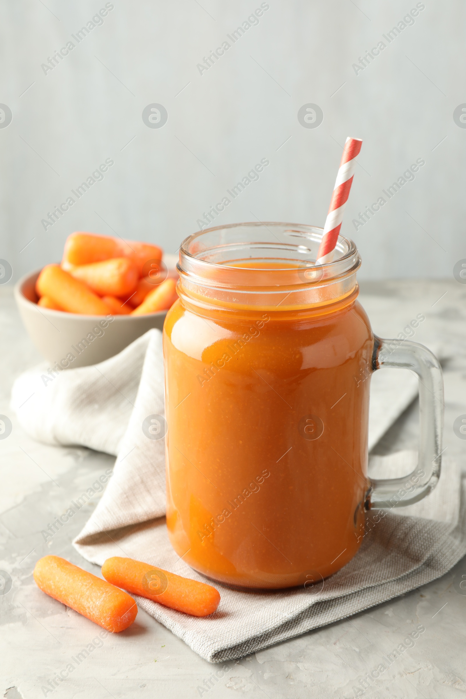 Photo of Fresh carrot juice in mason jar and vegetables on gray textured table