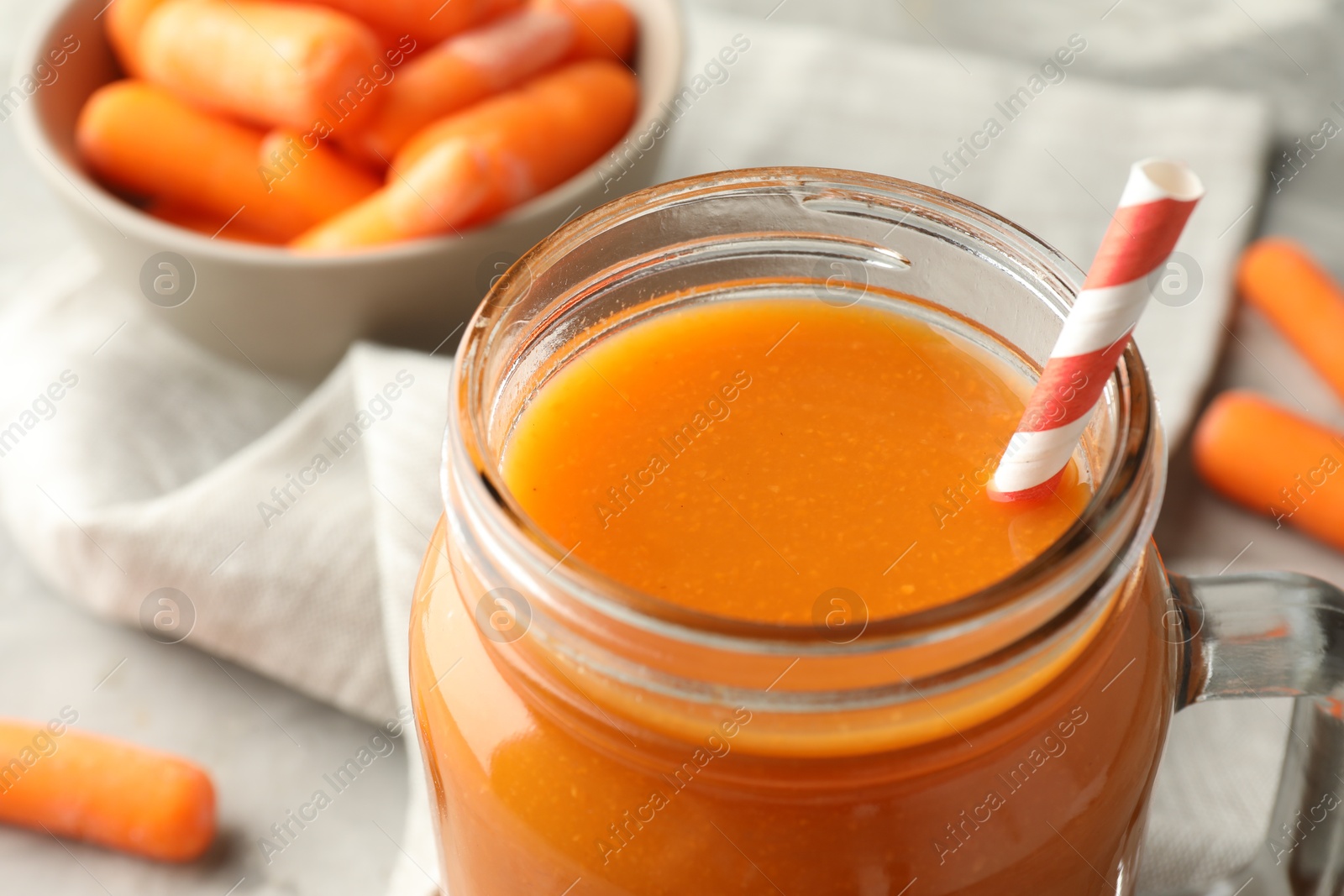 Photo of Fresh carrot juice in mason jar and vegetables on gray table, closeup