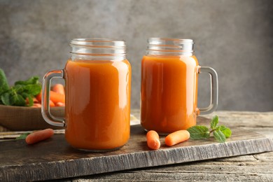 Photo of Fresh carrot juice in mason jars, vegetables and mint on wooden table against gray background