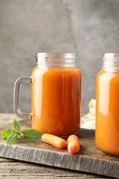 Photo of Fresh carrot juice in mason jars, vegetables and mint on wooden table against gray background