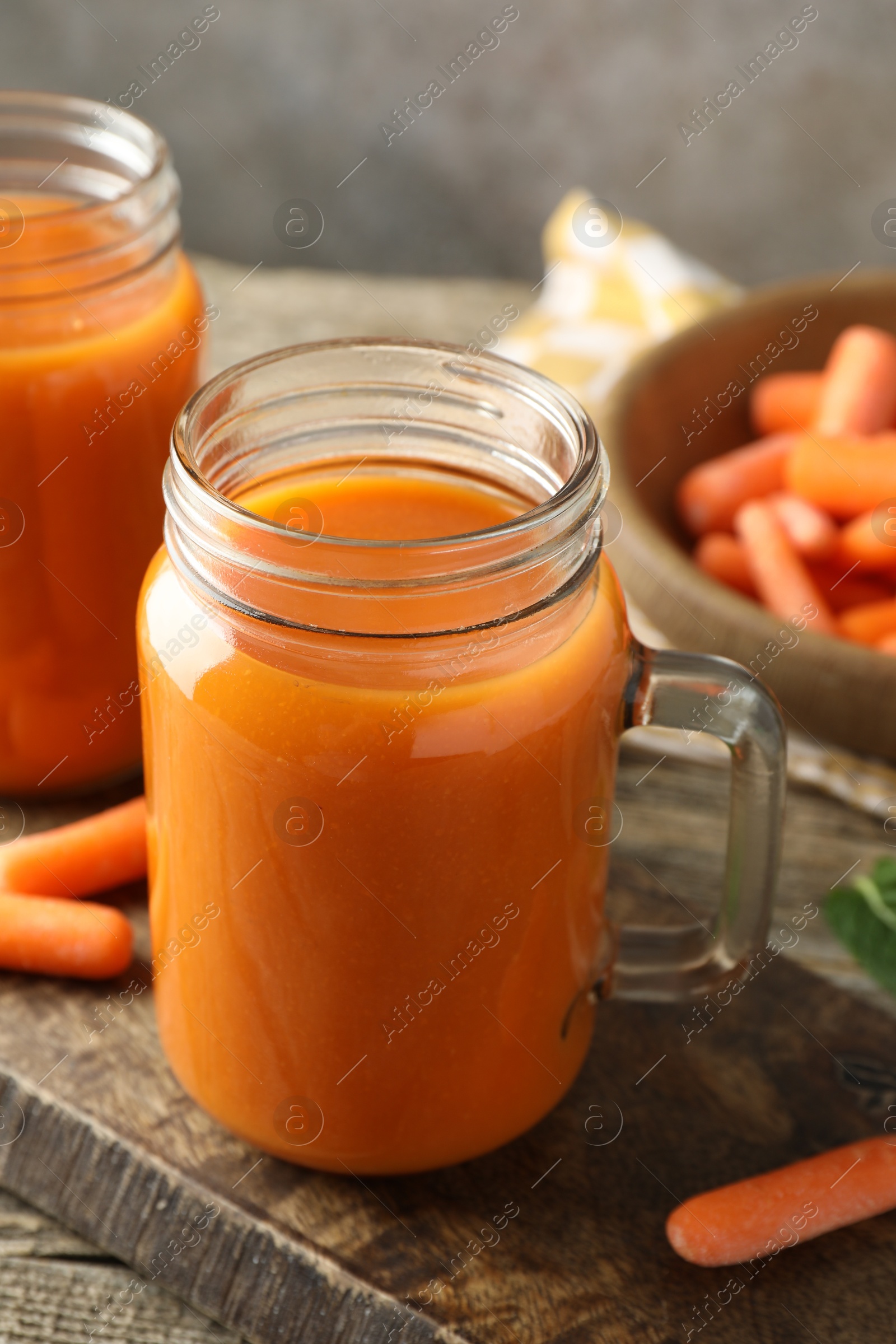 Photo of Fresh carrot juice in mason jars and vegetables on wooden table against gray background, closeup