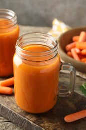 Photo of Fresh carrot juice in mason jars and vegetables on wooden table against gray background, closeup