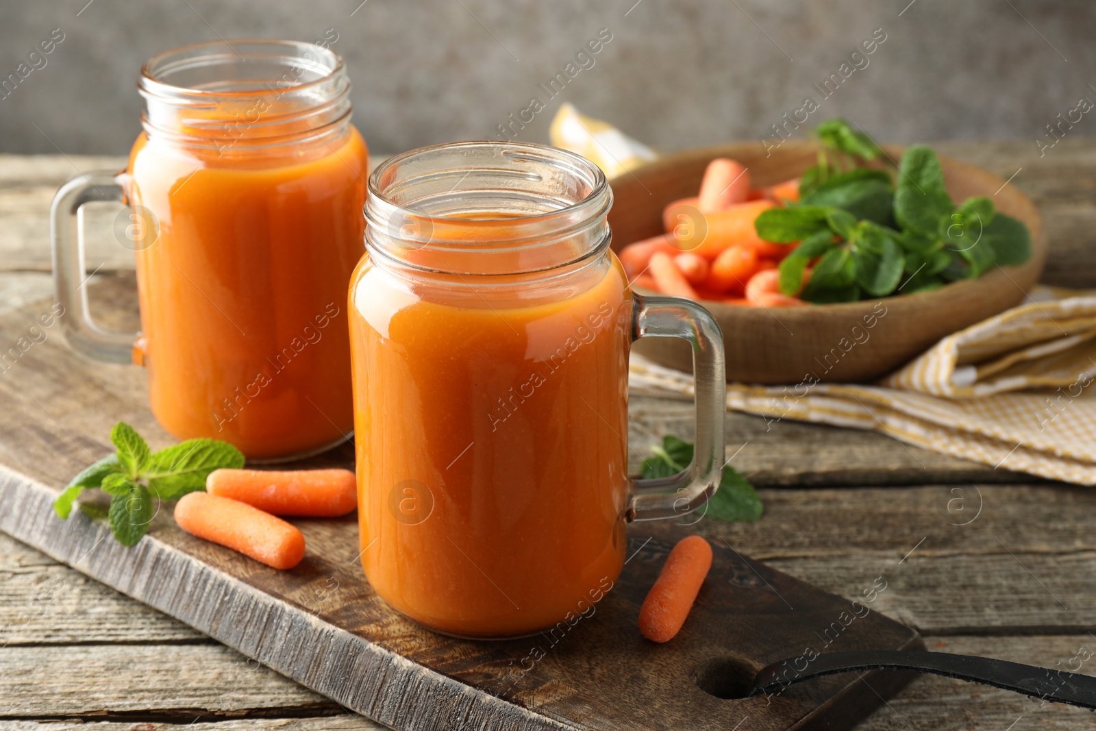 Photo of Fresh carrot juice in mason jars, vegetables and mint on wooden table