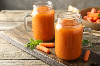 Photo of Fresh carrot juice in mason jars, vegetables and mint on wooden table, closeup